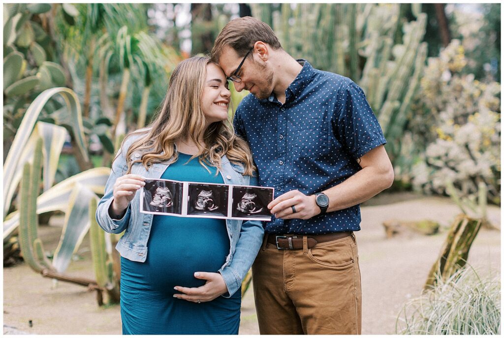 expecting parents cuddle up and hold 3 sonogram images of their baby