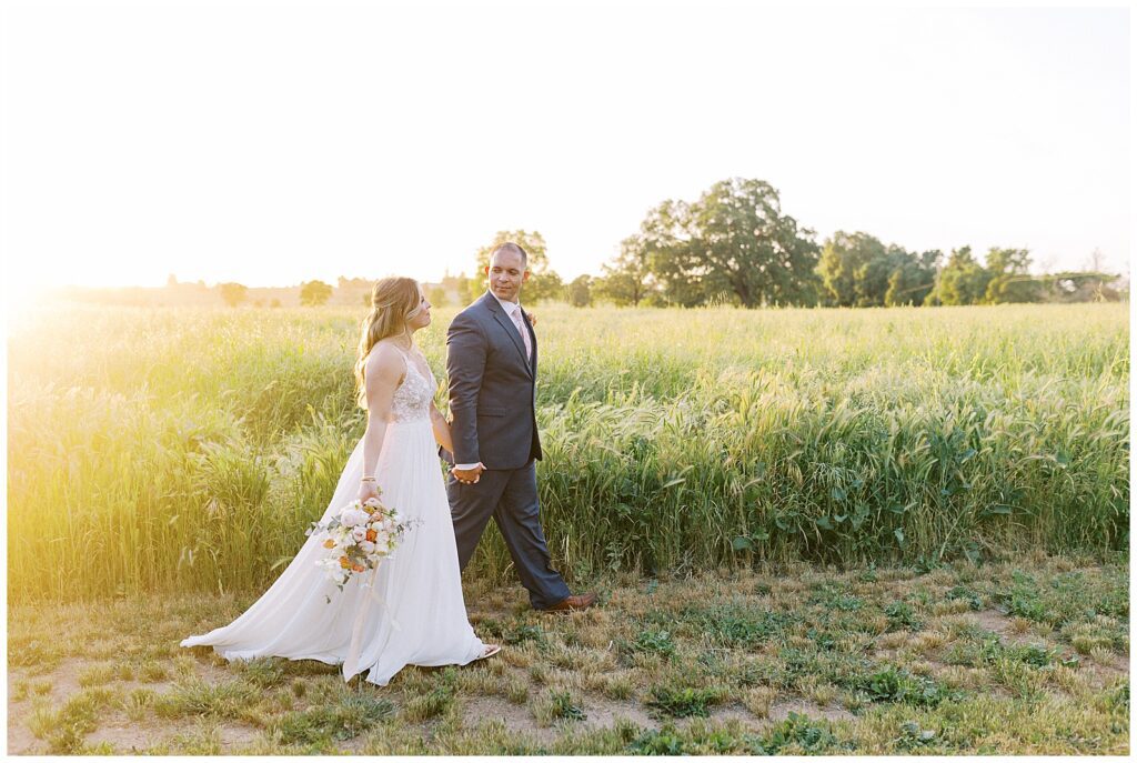 couple walking in front of a field of tall grass at their lamoure vineyard wedding