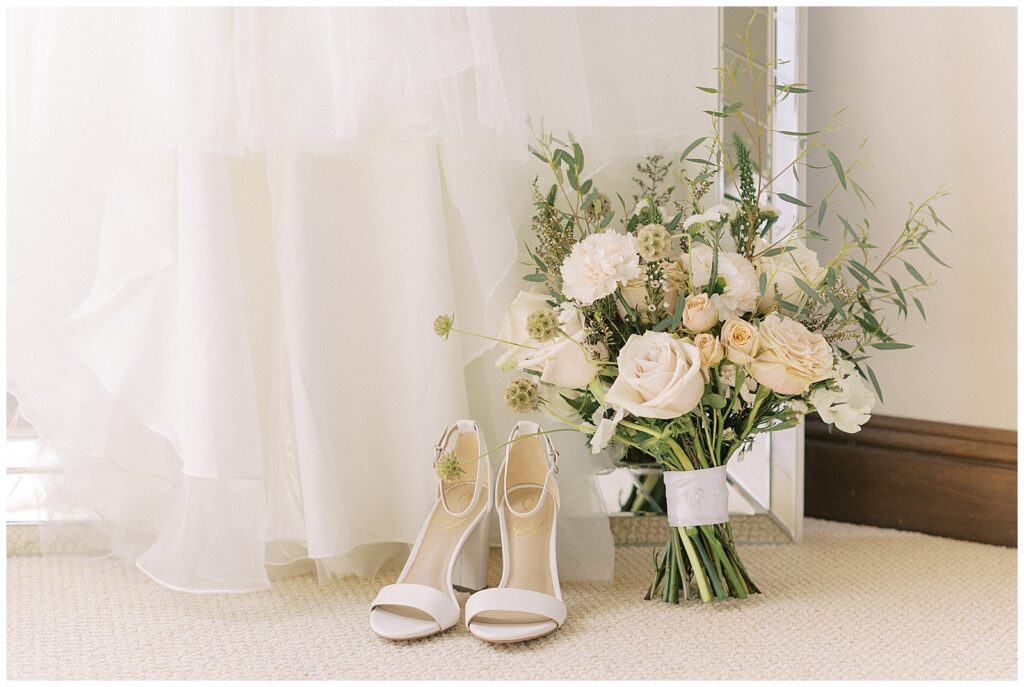 Bottom of the bride's wedding dress with her heels and wedding bouquet resting in front of it.