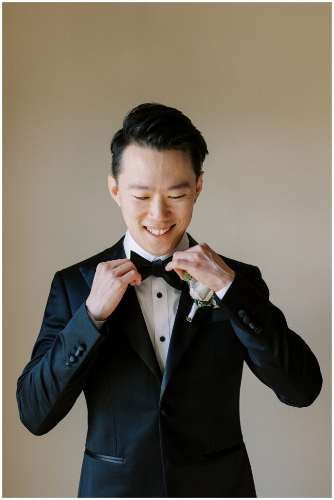 Groom adjusting his bowtie while getting ready.