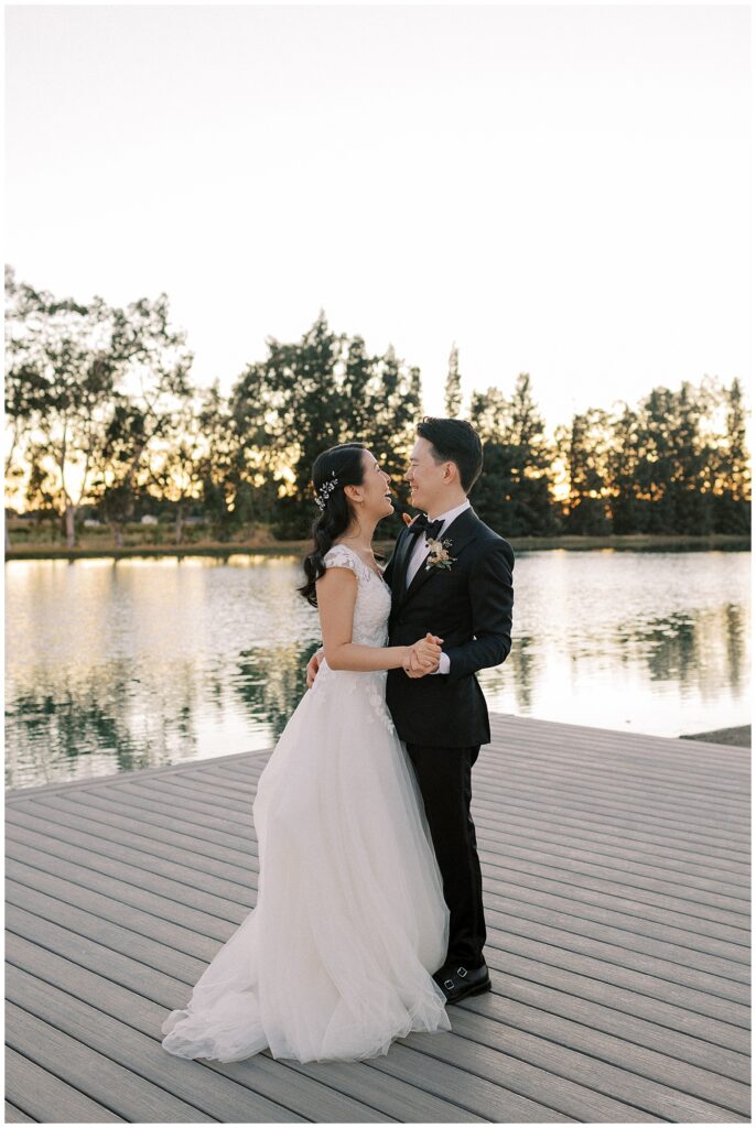 Bride and groom dancing in front of a lake during sunset.