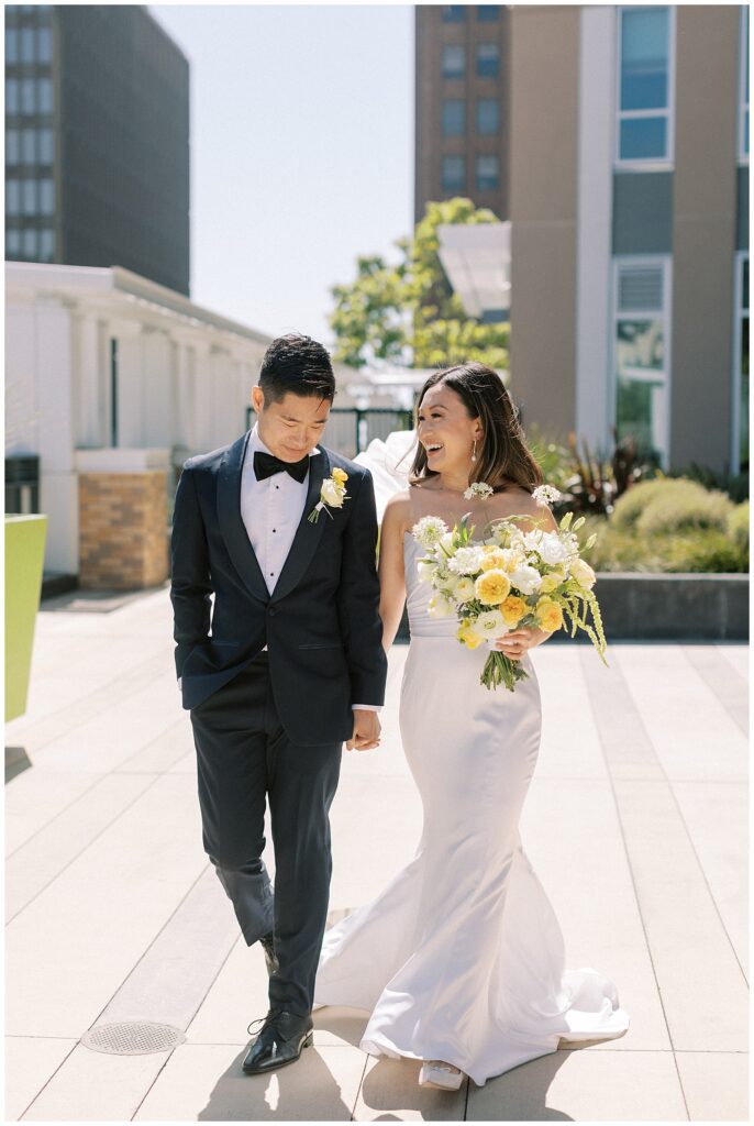 Bride and groom holding hands, talking to each other while walking toward the camera.