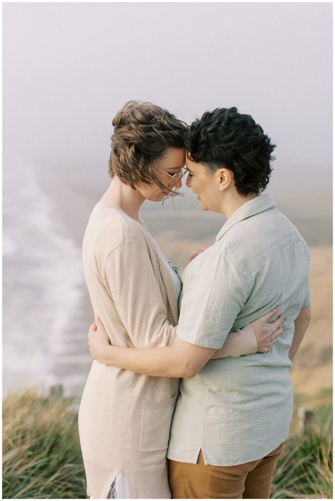 Engaged couple resting their foreheads together with a view of the ocean in the background