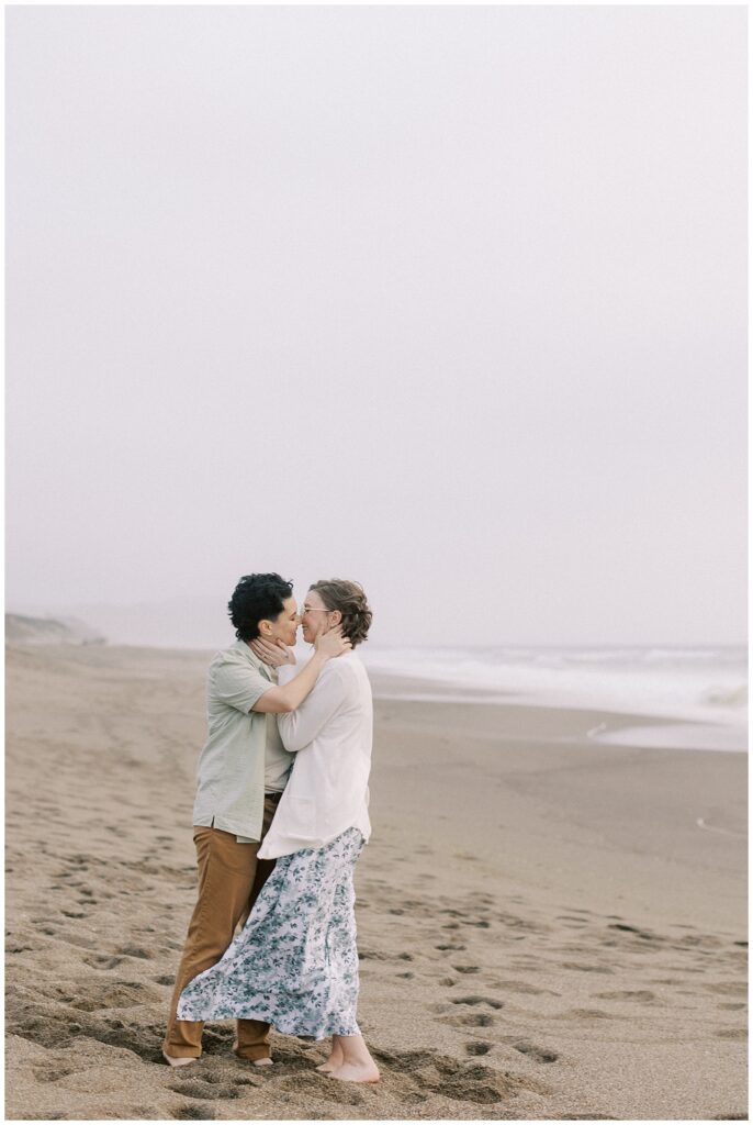 Engaged couple kisses on the sand in front of the ocean