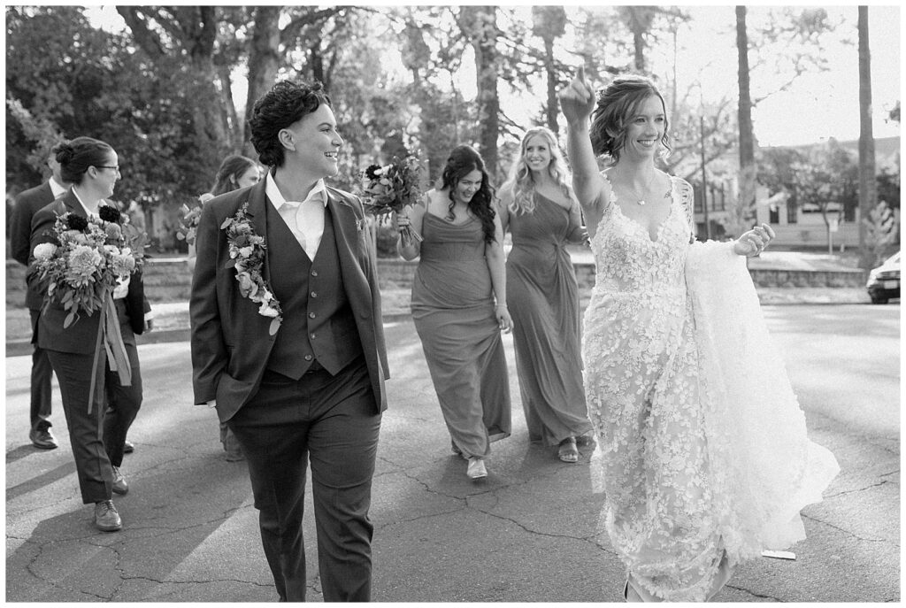 Black and white image of brides walking in front of their wedding party.